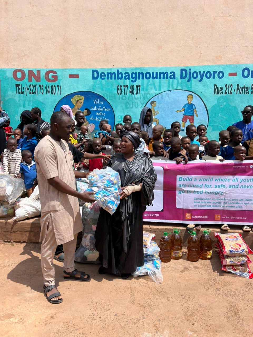 The handover of a bag of hygiene supplies to the orphanage director in front of the MACONA banner